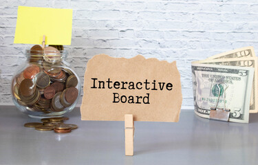 Business concept. Text INTERACTIVE BOARD on notebook with compass and paper clips on wooden table background.