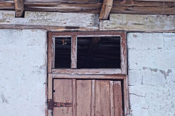 Sticker - one old small wooden brown window without glass above the door on a gray concrete wall of a house on the street