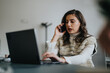 © qunica.com - Brunette woman discussing with client via phone call while working on lap top at the office.
