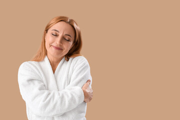 Wall Mural - Mature woman in bathrobe hugging herself on beige background