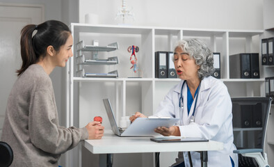 Wall Mural - An elderly Asian doctor is talking to a younger Asian woman across a desk in a medical office, monthly health check appointment.