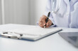 © M+Isolation+Photo - Medical doctor person hand is writing on a medical form on clipboard, on a white surface at medical desk.