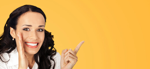 Sticker - Happy excited smiling businesswoman keep hand near face, showing indicating copy space. Amazed business woman covering mouth with palm, pointing away side by index finger, isolated yellow. Wide banner