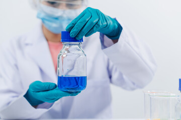 A scientist examines samples with a microscope in a laboratory with test tubes filled with colorful liquids in the background.