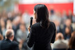 a woman speaking in front of crowd people bokeh style background