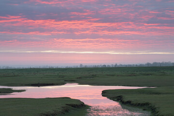Wall Mural - golden sunset over farm fields and small lake. colorful clouds reflect in the water
