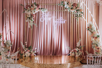 A beautifully decorated place for the wedding ceremony of the bride and groom in a modern style. Wedding arch made of white and pink fresh flowers. Beautiful decorative chairs and gilded legs