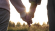 Close up silhouette of palms hands of elderly old people with wrinkles. Married couple of old people holding hands. Helping hand and support, feeling of love. Summer evening in park against sunset ray