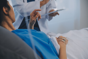 The senior woman specialist doctor with stethoscope checking up happy young Asian female patient lying in bed with receiving an intravenous saline drip in recovery room. Healthcare, medical insurance.