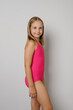© millaf - Attractive kid child girl in pink swimsuit standing on light gray studio wall background. Travel, sport, swimming activities and vacations concept