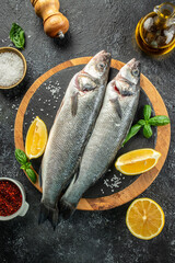 Wall Mural - raw fish sea bass with ingredients on a dark background. vertical image. top view. place for text