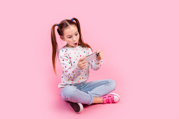 Poster - Full size photo of impressed schoolgirl dressed dotted pullover sit play in video game on smartphone isolated on pink color background