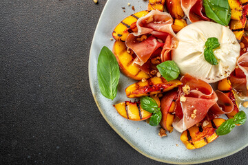 Wall Mural - Heathy summer salad with grilled peach, ham and burrata on a dark background. top view. copy space for text