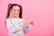 Portrait of cheerful schoolgirl with ponytails dressed dotted shirt indicating at discount empty space isolated on pink color background