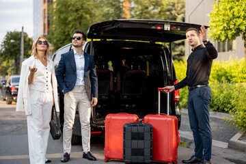 Wall Mural - Business couple standing by a minivan taxi waiting for their chauffeur or porter to help them with a suitcases. Concept of business trips and travel