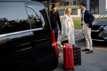 Business couple standing by a minivan taxi waiting for their chauffeur or porter to help them with a suitcases. Concept of business trips and travel