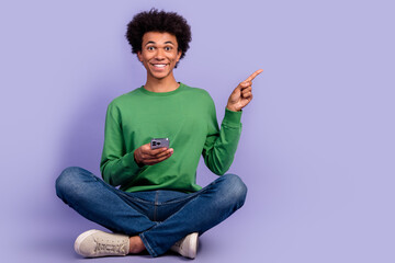 Poster - Full length photo of cheerful cute man dressed green sweater texting modern device pointing empty space isolated violet color background