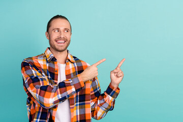 Photo of cheerful man with long hairstyle dressed checkered shirt look directing at promo empty space isolated on teal color background