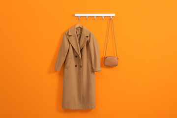 Wall Mural - Hanger with beige coat and bag on orange wall