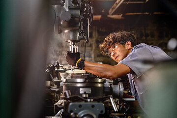 Wall Mural - Asian worker in production plant drilling at machine. Professional worker near drilling machine on factory. finishing metal working internal steel surface on lathe grinder machine with flying sparks.