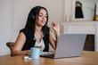 © Iona - Engaged businesswoman with headphones using laptop and enjoying coffee in a stylish workspace.