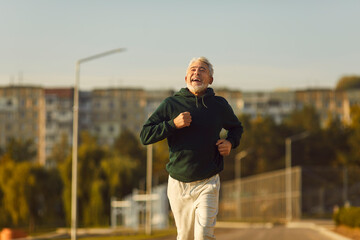 Wall Mural - Cheerful fit senior man enjoying jogging workout. Portrait happy smiling handsome bearded 60 - 70 year old man running on city street on sunny summer morning. Sport, fitness, healthy lifestyle concept