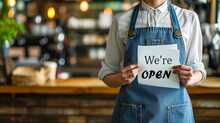 A Woman Wearing Apron And Jean Holding Paper With Text We Are Open At Customer Cafe Restaurant Bar Counter, Small Business Start Up Service Concept