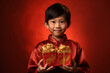 Asian cute boy holding angpao or red packet monetary gift and gold ingot isolated on red background. Happy Chinese new year.