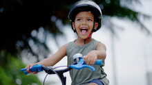 Portrait Little Cute Adorable Mixed Race Toddler Boy In Safety Helmet Enjoy Having Fun Riding Exercise Bike In City Park Road Yard Garden Forest. Child First Bike. Kid Outdoors Sport Summer Activities