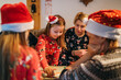© Soloviova Liudmyla - Mother with daughters kids playing together in table board game, wearing Christmas hats. Cozy pre Christmas evening time moment. Family values, board games and X-mas celebration concept.