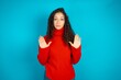 Serious beautiful teen girl wearing red knitted sweater pulls palms towards camera, makes stop gesture, asks to control your emotions and not be nervous