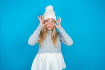 Wall Mural - Teen caucasian girl wearing blue knitted sweater and woolly hat keeping eyes opened to find a success opportunity.