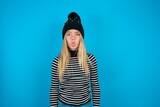 Fototapeta  - Teen caucasian girl wearing striped sweater and woolly hat making fish face with lips, crazy and comical gesture. Funny expression.