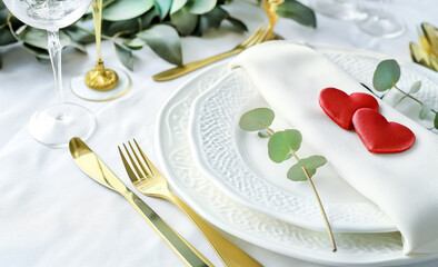 Valentines day or wedding dinner with table place setting with red hearts, golden cutlery and eucalyptus sprig on white background. Valentine's card.