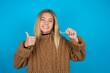 Teen caucasian girl wearing brown knitted sweater holding an invisible braces aligner and rising thumb up, recommending this new treatment. Dental healthcare concept.