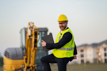 Wall Mural - Construction manager in suit and helmet at a construction site. Construction manager worker or supervisor wearing hardhat in front of house. Supervisor construction manager near excavator. Renovation.