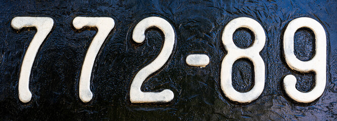 Weathered numbers 7, 2; 8, 9, seven, two, eight, nine, or 77289 painted white on a piece of black metal. Abstarct numeral background.