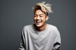 Portrait of a happy young asian man laughing against grey background