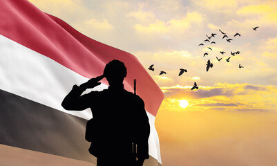 Silhouette of a soldier with the Yemen flag stands against the background of a sunset or sunrise. Concept of national holidays. Commemoration Day.