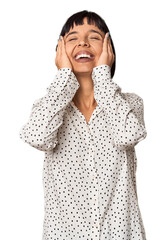 Wall Mural - Young Hispanic woman with short black hair in studio laughs joyfully keeping hands on head. Happiness concept.