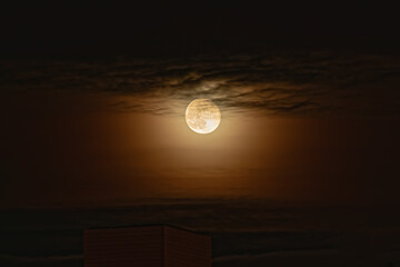 Wall Mural - The full moon in the sky is hidden in dark clouds. The Moon surrounded by an orange glow is diffuse moonlight in the atmosphere