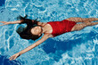 © SHOTPRIME STUDIO - Young woman in the pool in red swimsuit with a beautiful smile lying on the water and swimming in the blue pool in the sun, the concept of relaxing on vacation.