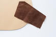 piece of brown pigskin leather and thin plywood sheet with clean, laser cut edges on white paper