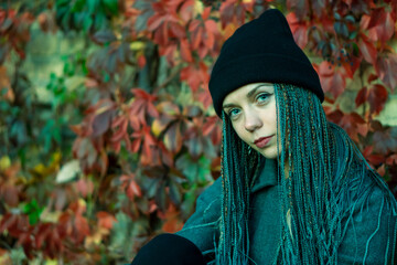 Portrait of a young beautiful girl with a smile on her face in an autumn park against a background of colorful leaves. A girl with dreadlocks and pigtails poses against the background of trees.