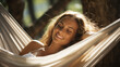 Happy woman is resting in hammock with her eyes closed and her hands behind her head smiling happily enjoying the day