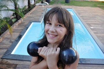 menina fazendo exercicios fitness com pesos alteres de academia em area externa de piscina 