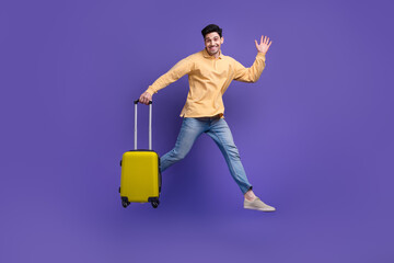 Canvas Print - Full size photo of attractive young man jumping run wave hand suitcase dressed stylish yellow clothes isolated on purple color background