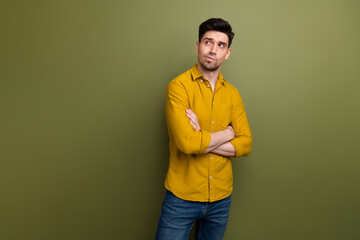 Portrait of minded pensive young man crossed arms look interested empty space brainstorming isolated on khaki color background