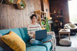 Full body photo of nice young lady sitting comfy couch use wireless laptop coworking chatting living room indoors