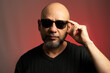 White, bald man, wearing sunglasses, confident and serious looking towards the camera.